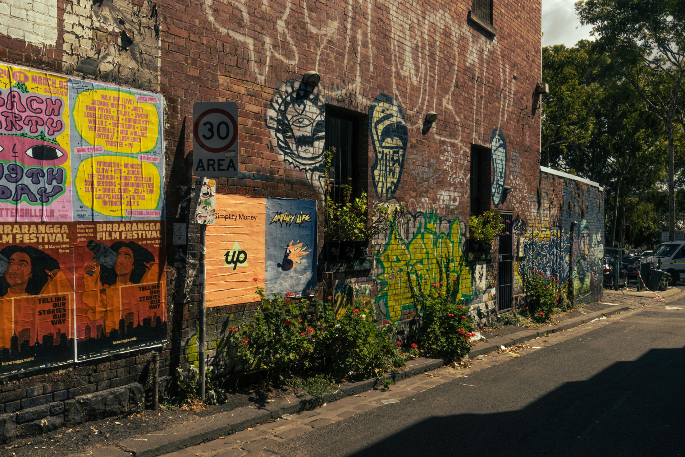 A brick wall with advertisements, graffiti and flowers on it