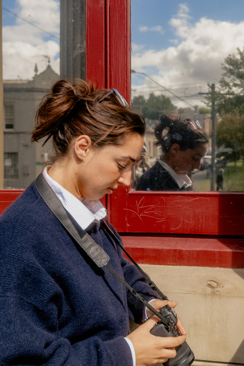 A woman looking down at her camera with a red window behind her